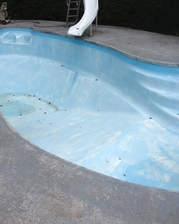 A fiberglass pool shell before refinishing, the blue gel coat faded and chalked unevenly.
