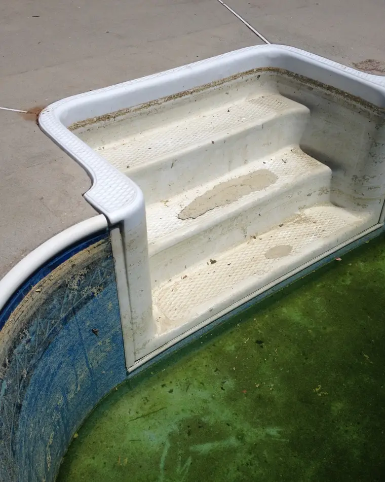 A moulded pool step unit before refinishing, its treads stained brown and the gel coat worn through in patches.