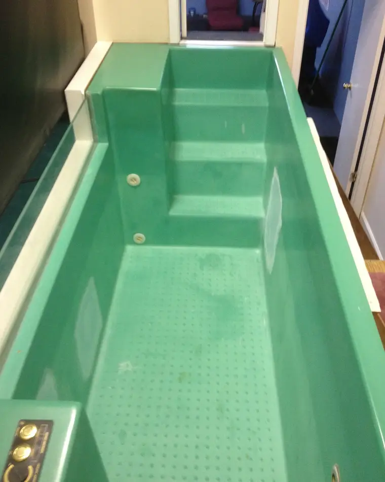 A fiberglass baptismal pool before refinishing, its moulded shell, steps and floor stained a worn green throughout.