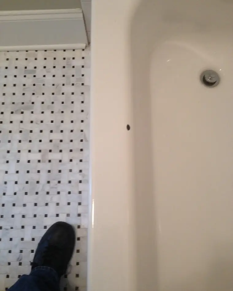 A bathtub apron before repair, with a dark chip broken through the finish.