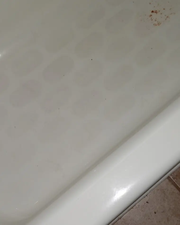 The floor of a bathtub before refinishing, with worn non-slip pads, dulled patches and rust flecks near the rim.